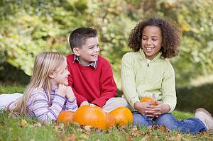 Three young friends sitting on grass with pumpkins smiling