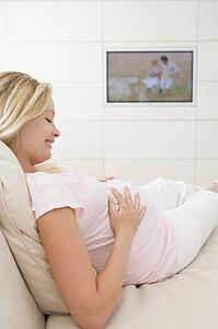 Pregnant woman watching television smiling