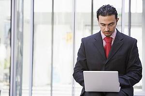 Businessman sitting outdoors by building with a laptop (high key/selective focus)