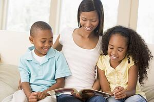 Woman and two children sitting in living room reading book and smiling
