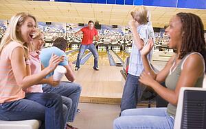 Family in bowling alley with two friends cheering and smiling