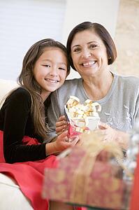 Grandmother And Granddaughter Sitting On Sofa Holding A Christmas Gift