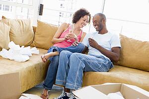 Couple relaxing with champagne by boxes in new home smiling