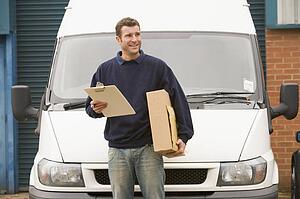Deliveryperson standing with van holding clipboard and box smiling