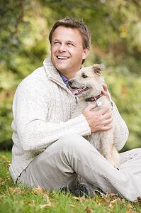 Man sitting outdoors with dog in park smiling (selective focus)