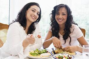 Two women sitting at dinner table smiling (high key)