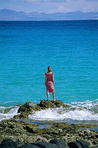 Woman outdoors standing on large rocks by the ocean