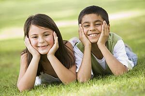Two young children outdoors lying in park smiling (selective focus)