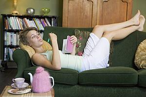 Young woman lying on sofa at home writing in her diary