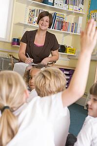 Teacher in class with student volunteering in foreground (selective focus)