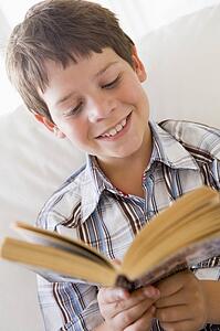 Young Boy Sitting On A Sofa Reading A Book