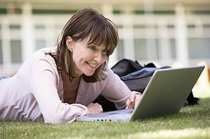 Woman lying on lawn of school with laptop