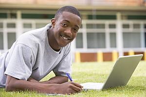 Student lying outdoors on lawn with laptop