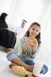 Young girl with fast food in living room smiling with parents in background (high key/selective focus) 