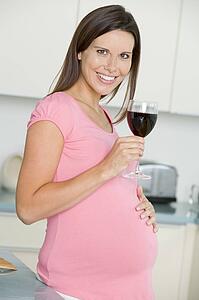 Pregnant woman in kitchen with glass of red wine smiling