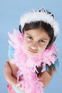 Young girl wearing crown and feather boa frowning