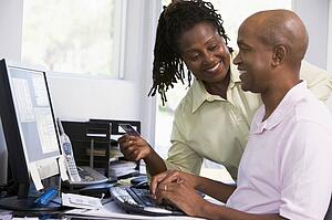 Couple in home office with credit card using computer and smiling