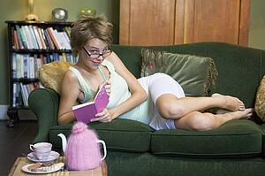 Young woman lying on sofa at home writing in her diary