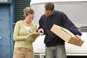 Two deliverypeople standing with van holding clipboard and box