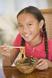 Young girl in dining room eating chinese food smiling