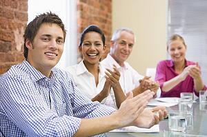 Four businesspeople in boardroom applauding and smiling