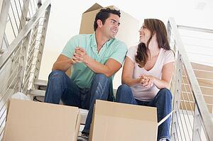 Couple sitting on staircase with boxes in new home smiling