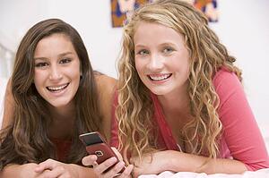 Teenage Girls Lying On Bed Using Mobile Phone