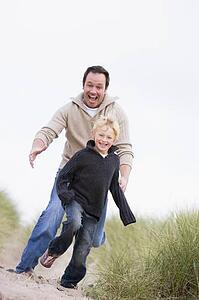 Father and son running on beach smiling