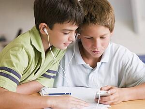 Two Young Boys Distracted From Their Homework, Playing With An MP3 Player