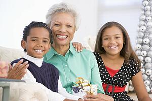 Grandmother Sitting With Her Two Grandchildren, Holding A Christmas Gift