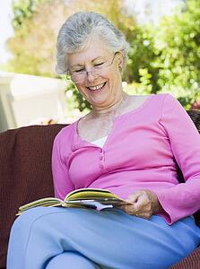 Senior woman sitting outdoors on a chair reading a book