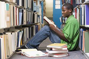 Man sitting on floor in library reading book