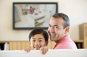 Man and young boy in living room with flat screen television smiling