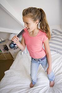 Young Girl Standing On Her Bed, Singing Into Her Hairbrush