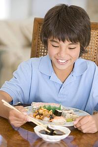 Young boy in dining room eating chinese food smiling