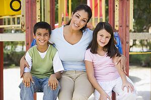 Mother and two young children sitting on playground structure smiling (selective focus)