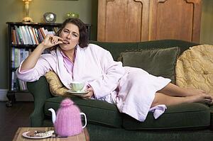 Young woman lying on sofa at home eating cookies and drinking tea