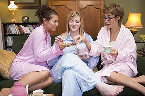 Three woman in night clothes sitting at home eating cookies and drinking tea