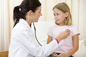 Doctor giving checkup with stethoscope to young girl in exam room