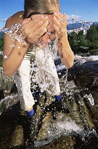 Woman outdoors by river splashing water on face (selective focus)