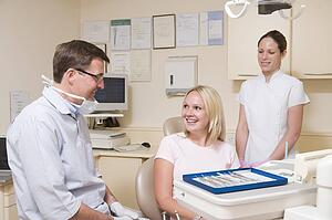 Dentist and assistant in exam room with woman in chair smiling