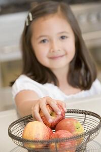 Young girl in kitchen getting apple off counter smiling