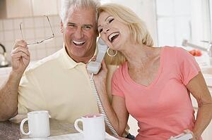 Couple in kitchen using telephone together and laughing