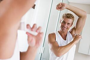Man in bathroom applying deodorant smiling