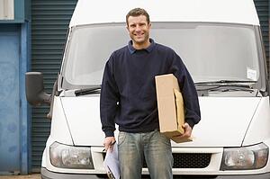 Deliveryperson standing with van holding clipboard and box smiling