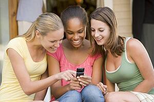 Teenage Girls Sitting Outside Playing With Mobile Phone