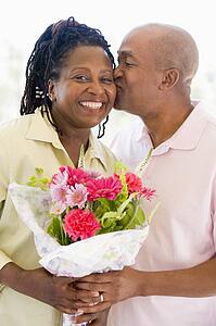 Husband and wife holding flowers kissing and smiling