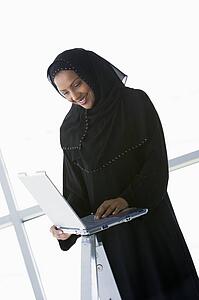 Woman indoors standing with laptop and smiling (high key/selective focus) 
