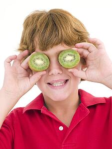 Young boy holding kiwi halves over eyes smiling