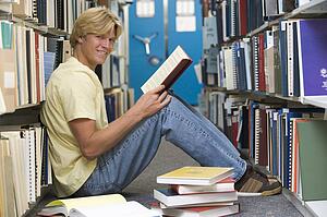 Man sitting on floor in library holding book
